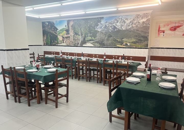 Comedor de El Chumarru: mesas con mantel verde, sillas de madera y un mural de un pueblo de montaña en la pared del fondo.