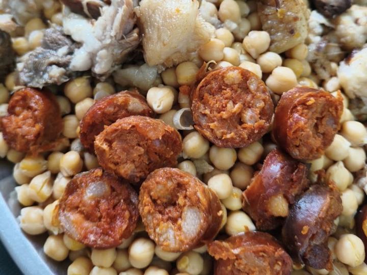 Garbanzos con rodajas de chorizo y las carnes del cocido, servidos en una fuente.