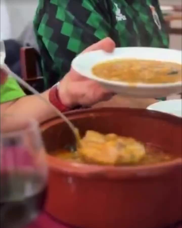 Un cucharón sirve el cocido de la cazuela de barro al plato, en una mesa del comedor.